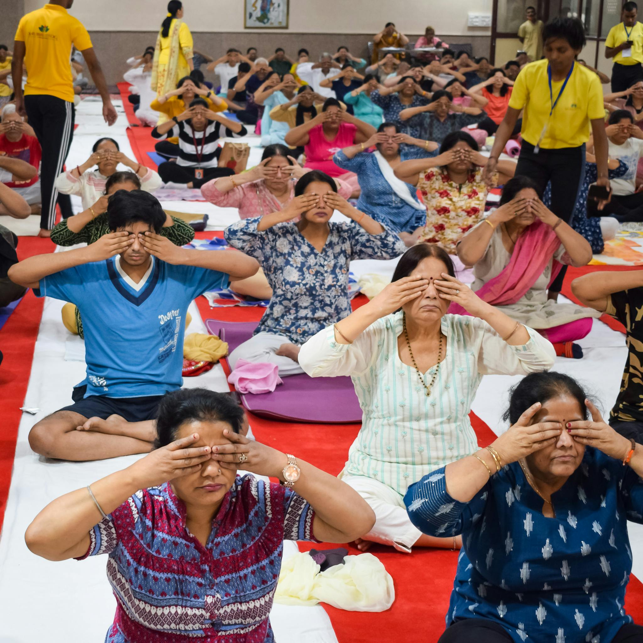 A large group of adults engaged in a meditation class, practicing mindfulness exercises indoors.